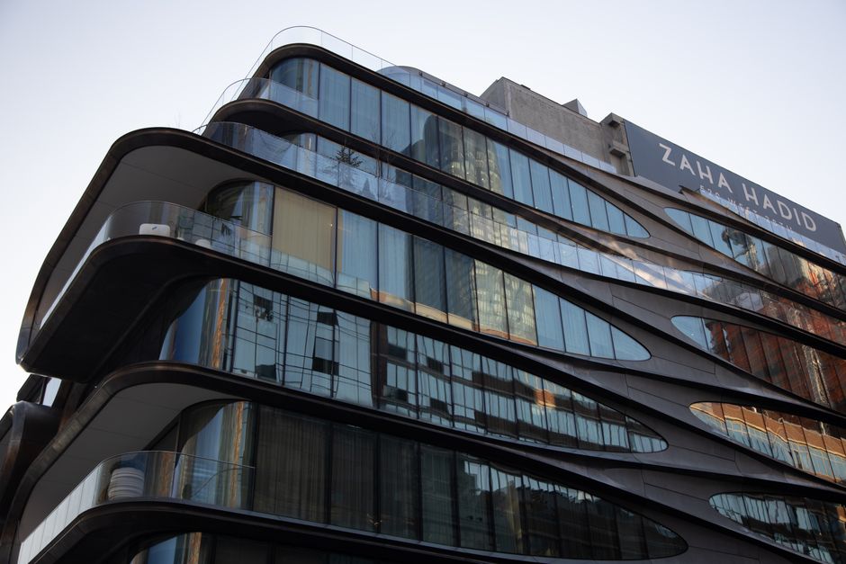 A modern multi-storey commercial building with a distinctive curved glass façade reflecting nearby structures and the sky, featuring large tinted glass windows and sleek black paneling. The building'